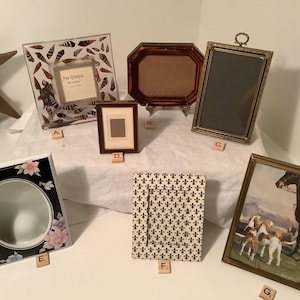 May include: A collection of seven assorted picture frames labeled A through G. The frames vary in shape, size, and design, including a shell-patterned square, a dark wood octagon, a metallic rectangle, a floral ceramic frame, and a horse print.