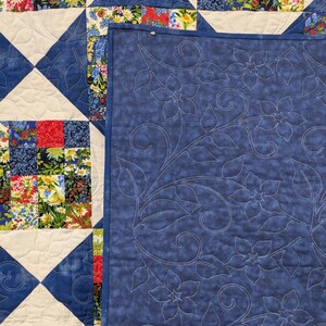 May include: A handmade quilt with a patchwork design featuring squares of floral fabric in red, blue, and white. The quilt has a blue and white diamond pattern and a solid blue backing with floral embroidery.