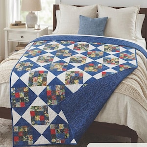 May include: A blue and white quilt with a patchwork design, featuring squares of floral fabric. The quilt is draped over a bed, showcasing its diamond pattern. Finished size is 55.5" x 71.5".