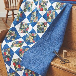 May include: A handmade quilt with a blue and white geometric pattern. The quilt features floral squares and a solid blue backing. A pair of scissors and thread are on the wooden surface.