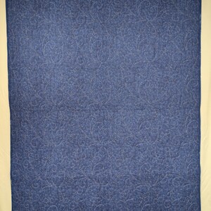 May include: A blue quilt with a floral pattern. The quilt is a solid blue color with a detailed, repeating floral design stitched throughout. The quilt is hanging from black clips.