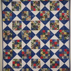 May include: A handmade quilt with a repeating pattern of squares and diamonds. The quilt features a combination of floral fabric squares in red, yellow, and blue, set against a white and blue background. The quilt is a cozy and decorative textile.