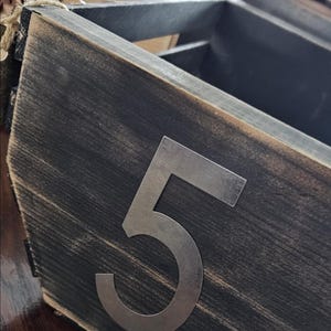 Peut inclure: Une boîte en bois rustique avec une finition gris foncé vieillie. Un grand chiffre 5 en métal argenté est fixé à l'avant. La boîte fait partie d'un ensemble, avec d'autres boîtes visibles en arrière-plan.