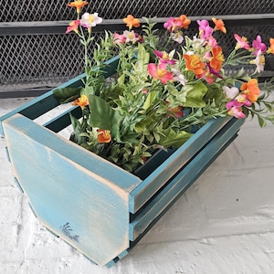 Peut inclure: Un bac en bois peint en bleu turquoise rempli de fausses fleurs colorées. Les fleurs sont un mélange d'orange, de rose et de blanc, avec du feuillage vert. Le bac a une finition vieillie et mesure environ 30 cm de long.