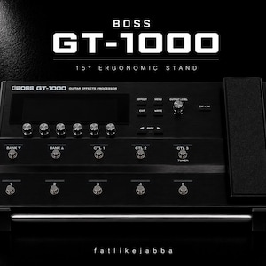 以下が含まれることがあります： 15度の人間工学に基づいたスタンドに設置された黒いBOSS GT-1000ギターエフェクトプロセッサー。デジタルディスプレイ、複数のコントロールノブ、1から5までの5つのフットスイッチ、バンクおよびコントロールスイッチ、エクスプレッションペダルを備えています。