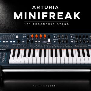 Könnte beinhalten: Der Arturia Minifreak Synthesizer steht auf einem schwarzen, 15 Grad geneigten ergonomischen Ständer. Das dunkelgraue Keyboard verfügt über weiße und schwarze Tasten, zahlreiche schwarze und orangefarbene Drehregler, ein kleines Display und blaue Leuchten.