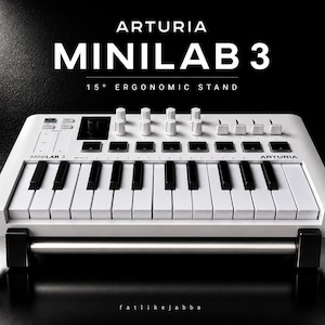 以下が含まれることがあります： 15度の人間工学に基づいた黒いスタンドに置かれた白いArturia MiniLab 3 MIDIキーボード。このデバイスは、白と黒の鍵盤、複数の白い回転ノブ、スライダー、パッドを備えており、Arturia MiniLab 3というテキストが表示されています。