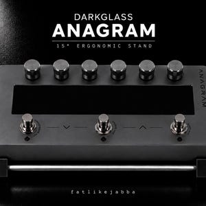 Könnte beinhalten: Ein dunkelgrauer Darkglass Anagram 15° ergonomischer Ständer mit einem rechteckigen Metallrahmen, sechs Drehreglern, drei Fußschaltern und dem Text "DARKGLASS ANAGRAM 15° ERGONOMIC STAND" sowie "ANAGRAM" auf der Oberfläche.