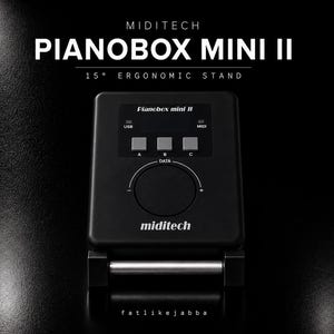 May include: A black Miditech Pianobox Mini II sound module featuring a central data dial, three square buttons labeled A, B, and C, and a top display area. The device is mounted on a 15-degree ergonomic stand with a silver horizontal support bar.