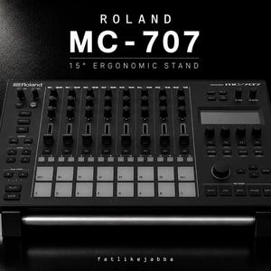 May include: A black Roland MC-707 groovebox resting on a 15-degree ergonomic stand. The device features numerous knobs, sliders, a digital display, and a grid of backlit pads. Text above reads ROLAND MC-707 15° ERGONOMIC STAND and below is fatlikejabba.