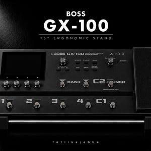 以下が含まれることがあります： 15度の人間工学に基づいたスタンドに設置された黒いBoss GX-100ギターエフェクトプロセッサー。デジタルディスプレイ、複数のコントロールノブ、1から4までのフットスイッチ、C1、C2、および右側に内蔵されたエクスプレッションペダルを備えています。