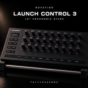 May include: A black Novation Launch Control 3, a 15-degree ergonomic stand. The device has numerous knobs and buttons, with the text "LAUNCH CONTROL 3" and "15° ERGONOMIC STAND" displayed. The device is on a black surface.