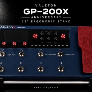Pode incluir: Um processador multiefeitos Valeton GP-200X azul escuro com um pedal de expressão vermelho, botões de controle vermelhos e vários interruptores de pé metálicos rotulados A, B, C e D. A unidade exibe o texto VALETON GP-200X ANNIVERSARY 15° ERGONOMIC STAND.