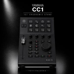 Puede incluir: Un controlador negro Yamaha CC1 15 degree ergonomic stand que presenta un fader vertical, una rueda de desplazamiento circular grande, múltiples botones cuadrados con iconos y texto, y una cuadrícula de teclas de función. El dispositivo está etiquetado como Yamaha CC1.