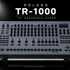 May include: A grey Roland TR-1000 Rhythm Creator drum machine mounted on a 15-degree ergonomic stand. The device features numerous black knobs, sliders, and buttons across its control panel, with the text ROLAND TR-1000 15° ERGONOMIC STAND visible.