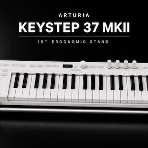 May include: A white Arturia KeyStep 37 MKII MIDI keyboard controller resting on a silver and black 15-degree ergonomic stand. The keyboard features black and white keys, various control buttons, knobs, and a small display screen on the top panel.