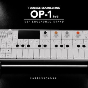 Könnte beinhalten: Ein Teenage Engineering OP-1 field Synthesizer auf einem 15 Grad ergonomischen Ständer. Das Gerät hat ein weißes Gehäuse, einen schwarzen Bildschirm, weiße Tasten und vier farbige Drehregler in Schwarz, Orange, Grau und Rot. Text OP-1 field.