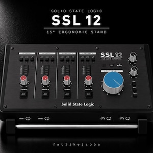 Puede incluir: Una interfaz de audio USB Solid State Logic SSL 12 negra sobre un soporte ergonómico de 15 grados. El dispositivo cuenta con cuatro canales con perillas de tapa roja, una perilla de nivel de monitor azul grande, botones y puertos.