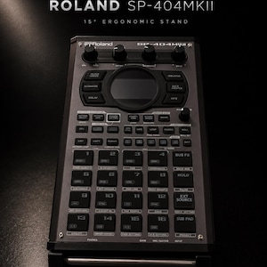 Peut inclure: Un échantillonneur Roland SP-404MKII noir et gris avec de nombreux boutons, des molettes et un écran central. Le texte "ROLAND SP-404MKII" et "15° ERGONOMIC STAND" sont visibles en haut. L'appareil a un design élégant et moderne.