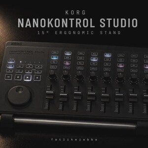 May include: A black Korg nanoKONTROL Studio mobile MIDI controller resting on a 15-degree ergonomic stand. The device features multiple sliders, rotary knobs, and illuminated buttons labelled Mute, Solo, Rec, and Select, with transport controls.