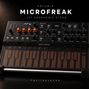 Könnte beinhalten: Ein schwarzer Arturia MicroFreak Synthesizer mit orangefarbenen Knöpfen und einer gemusterten Tastatur. Der Text "MICROFREAK" wird über der Tastatur angezeigt, darunter "15° ERGONOMIC STAND". Der Synthesizer hat ein schlankes, modernes Design.