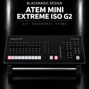 Puede incluir: Un mezclador de video negro Blackmagic Design ATEM Mini Extreme ISO G2 montado en un soporte ergonómico de 15 grados. El dispositivo cuenta con numerosos botones de control, perillas y un fader, con teclas iluminadas en blanco y rosa.