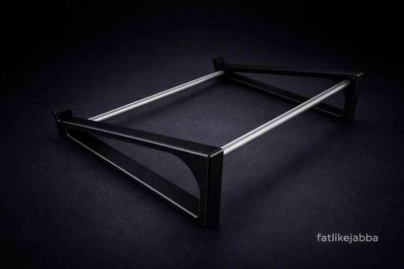 Puede incluir: Un soporte de metal negro con dos marcos laterales triangulares conectados por dos varillas met&aacute;licas horizontales de color plateado. El soporte tiene un dise&ntilde;o angular y elegante con un acabado mate. El texto fatlikejabba est&aacute; impreso en blanco.