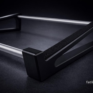 Puede incluir: Un soporte de metal negro y plateado con dos barras cil&iacute;ndricas plateadas paralelas conectadas por dos marcos laterales triangulares negros con bordes superiores texturizados. El texto fatlikejabba est&aacute; impreso en blanco abajo a la derecha.