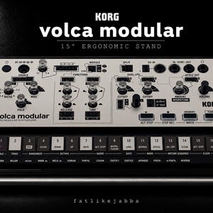 Puede incluir: Un sintetizador micro modular Korg Volca Modular sobre un soporte ergonómico de 15 grados. El dispositivo cuenta con un panel de control blanco con texto negro, numerosos mandos, puntos de conexión y un teclado táctil negro con dieciséis teclas.
