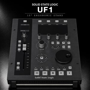 Op de afbeelding: Een zwarte Solid State Logic UF1 DAW-controller met een ergonomische standaard van 15 graden, een gemotoriseerde fader, een grote draaiknop, meerdere functieknoppen, transportbediening en een centraal display met witte tekstlabels.