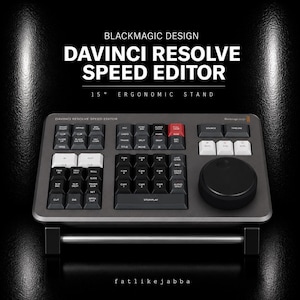 Op de afbeelding: Een donkergrijze Blackmagic Design DaVinci Resolve Speed Editor console met een raster van zwarte en witte toetsen, een grote ronde jog-wheel en een ergonomische standaard van 15 graden. Het apparaat bevat knoppen met labels voor functies.