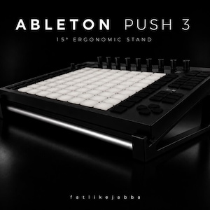 Könnte beinhalten: Ein schwarzer Ableton Push 3 Musikproduktions-Controller auf einem 15-Grad-Ergonomie-Ständer. Der Controller verfügt über ein Raster aus weißen Pads, schwarzen Tasten und Knöpfen. Der Text "ABLETON PUSH 3" steht oben.