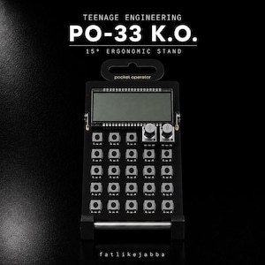 Könnte beinhalten: Ein schwarzer, 15 Grad geneigter ergonomischer Ständer für einen Teenage Engineering PO-33 K.O. pocket operator. Der Ständer verfügt über einen rechteckigen Rahmen mit einer oberen Aufhängeschlaufe, einer flachen Basis und einer silbernen Stange.