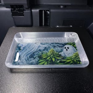 Może przedstawiać: Prostokątna, przezroczysta taca z kolorowym wzorem. Wzór przedstawia białego ducha, zielone rośliny i niebieskie wiry. Taca stoi na ciemnej powierzchni.