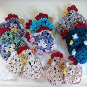 May include: A collection of handmade crochet chicken-shaped items in various colors. Each chicken has a red comb, yellow beak, and black eyes. The crochet work features a square pattern, and the chickens are arranged on a white surface.
