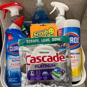 Może przedstawiać: Biały plastikowy pojemnik wypełniony środkami czyszczącymi. Zawiera płyn do czyszczenia toalet Clorox, gąbki Scrub Daddy, kapsułki do zmywarki Cascade Platinum, butelki z rozpylaczem i chusteczki dezynfekujące Clorox.