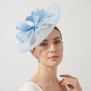 May include: A light blue hat with a large bow and a mesh brim. The hat is a stylish accessory, perfect for special occasions. The hat's design features a prominent bow and a delicate mesh material.