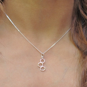 May include: A silver necklace with a pendant shaped like a honeycomb. The pendant is made of three connected hexagons.