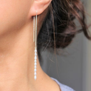 Peut inclure: Boucles d'oreilles en chaîne argent avec une rangée de perles blanches qui pendent du bas.