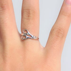 May include: A silver ring shaped like a pair of scissors.