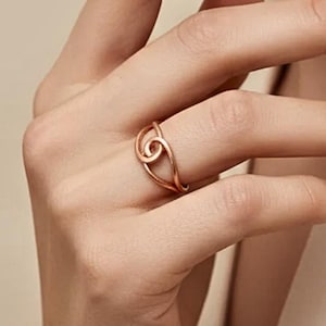 Peut inclure: Une bague en or rose avec un design en spirale unique. La bague est portée au doigt, mettant en valeur sa forme délicate et artistique. Le métal a une finition chaude et polie, reflétant la lumière.