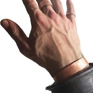 May include: Copper rings and a copper bracelet are displayed. The rings have different designs, one is a simple band, and the other is a braided design. The bracelet is a simple band. The text at the bottom of the image reads "Improves Vitality and Blood-Flow."