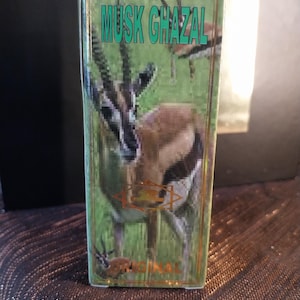 Może przedstawiać: Prostokątne pudełko na perfumy z zielonym tłem i wizerunkiem gazeli. Napis MUSK GHAZAL jest wydrukowany w kolorze morskim u góry, a słowo ORIGINAL jest wydrukowane złotą czcionką na dole. Pudełko posiada cienką złotą obwódkę.