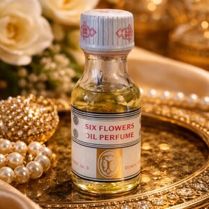 Może przedstawiać: Mała szklana butelka perfum w olejku Six Flowers z biało-czerwoną nakrętką. Etykieta zawiera napis "SIX FLOWERS OIL PERFUME" i złoty emblemat. Butelka jest wypełniona żółtym płynem i stoi na złotej tacy.