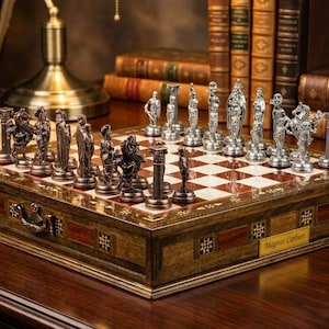 May include: A detailed chess set with silver-colored pieces on a wooden board. The board has a checkerboard pattern with red and white squares. The chess pieces are sculpted figures. The set is displayed on a dark wooden surface.