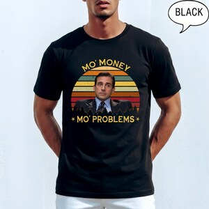 May include: Black t-shirt featuring a graphic of a man in a suit with the text "Mo' Money Mo' Problems" in a retro sunset design. The shirt is a crew neck style.