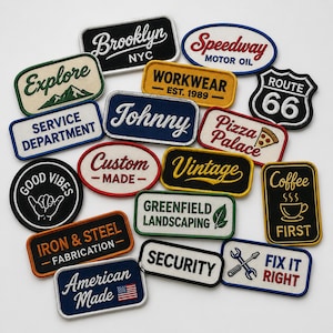 Op de afbeelding: Een verzameling van diverse geborduurde patches met uiteenlopende teksten en grafische ontwerpen, waaronder Brooklyn NYC, Speedway Motor Oil, Route 66, Explore, Workwear, Johnny, Pizza Palace, Good Vibes, Custom Made, Vintage, Coffee First, Iron & Steel, Greenfield Landscaping, Security, American Made en Fix It Right.