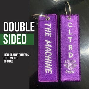 May include: Two purple, double-sided keyrings with silver rings. One reads "THE MACHINE" in white thread. The other reads "CLTRD ROLLER DERBY" in white thread. The image also includes the text "DOUBLE SIDED", "HIGH-QUALITY THREADS", "LIGHT WEIGHT", and "DURABLE".
