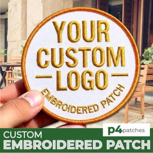 Könnte beinhalten: Ein runder, weißer, gestickter Aufnäher mit goldenem Text, der "YOUR CUSTOM LOGO" und "EMBROIDERED PATCH" lautet. Der Aufnäher hat einen goldenen Rand und wird von einer Hand gehalten. Der untere Teil des Bildes enthält den Text "CUSTOM EMBROIDERED PATCH".