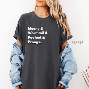 May include: Dark gray t-shirt with the text "Moony & Wormtail & Padfoot & Prongs." The shirt is a relaxed fit and has rolled-up sleeves. The word "PEPPER" is printed on the right side of the shirt.